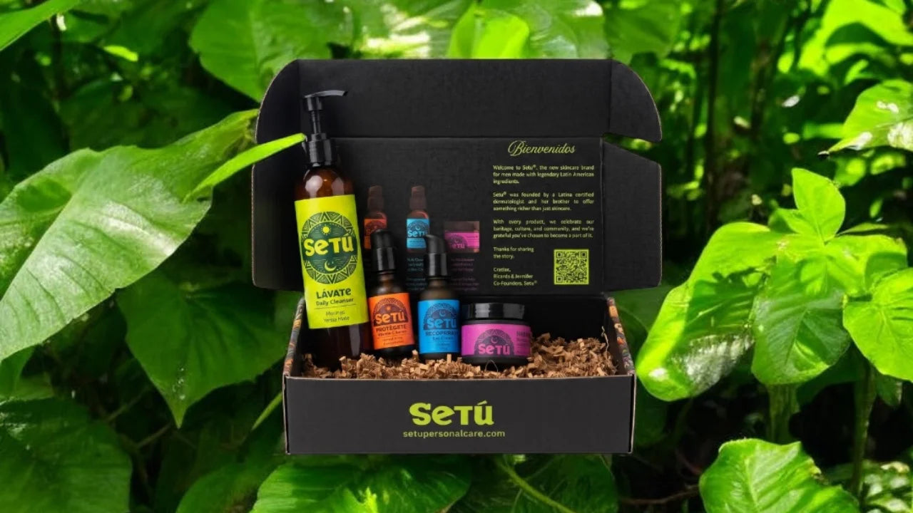 A Setu gift box filled with skincare and haircare products, photographed outdoors among lush green leaves. The open black box contains several bottles and jars with colorful labels