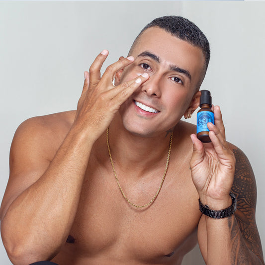 Man applying setu eye cream skincare product to face with a bottle in hand on a plain background