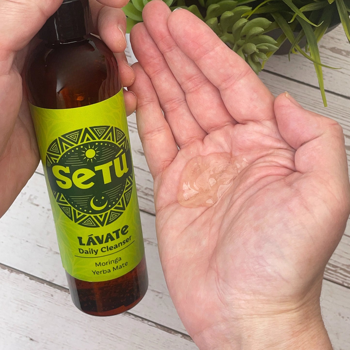 Setu Lávate Daily Cleanser bottle with a sample on a hand against a wooden background