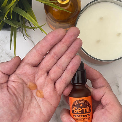 Person holding a bottle of 'Setu' skincare serum with a candle and plant in the background.