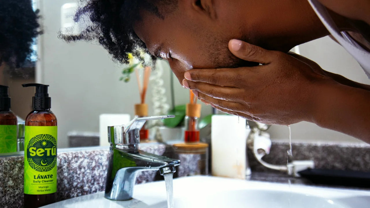 A person washing their face at a bathroom sink, with a Setu Lavate cleansing bottle visible on the counter in the foreground.