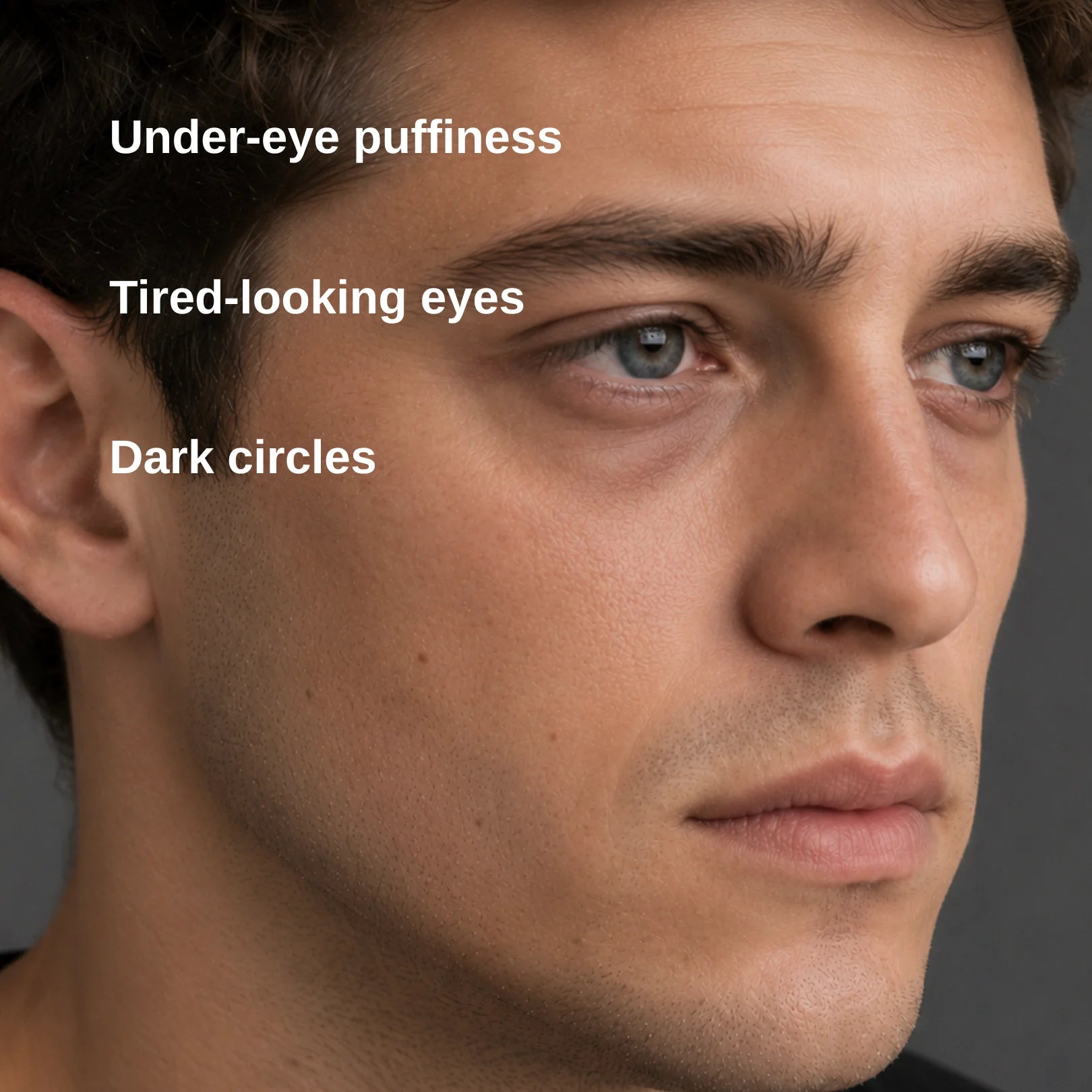 Close-up of a man's face with overlaid text reading 'Under-eye puffiness', 'Tired-looking eyes', and 'Dark circles' on a dark gray background.
