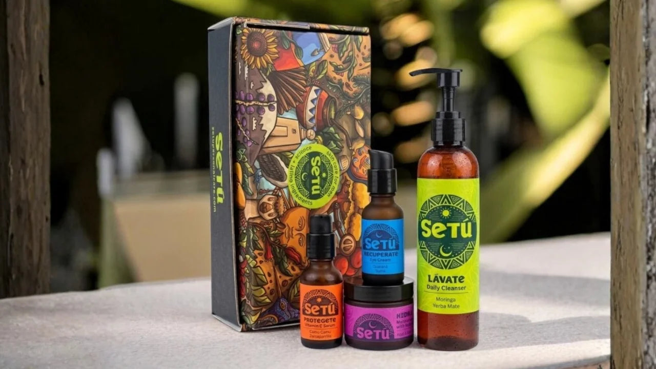 A Setu brand gift set featuring a large illustrated box and fourbottles: Lavate body cleanser, a small amber bottle, and a small jar with a black pump, displayed on a stone surface with a blurred outdoor background.
