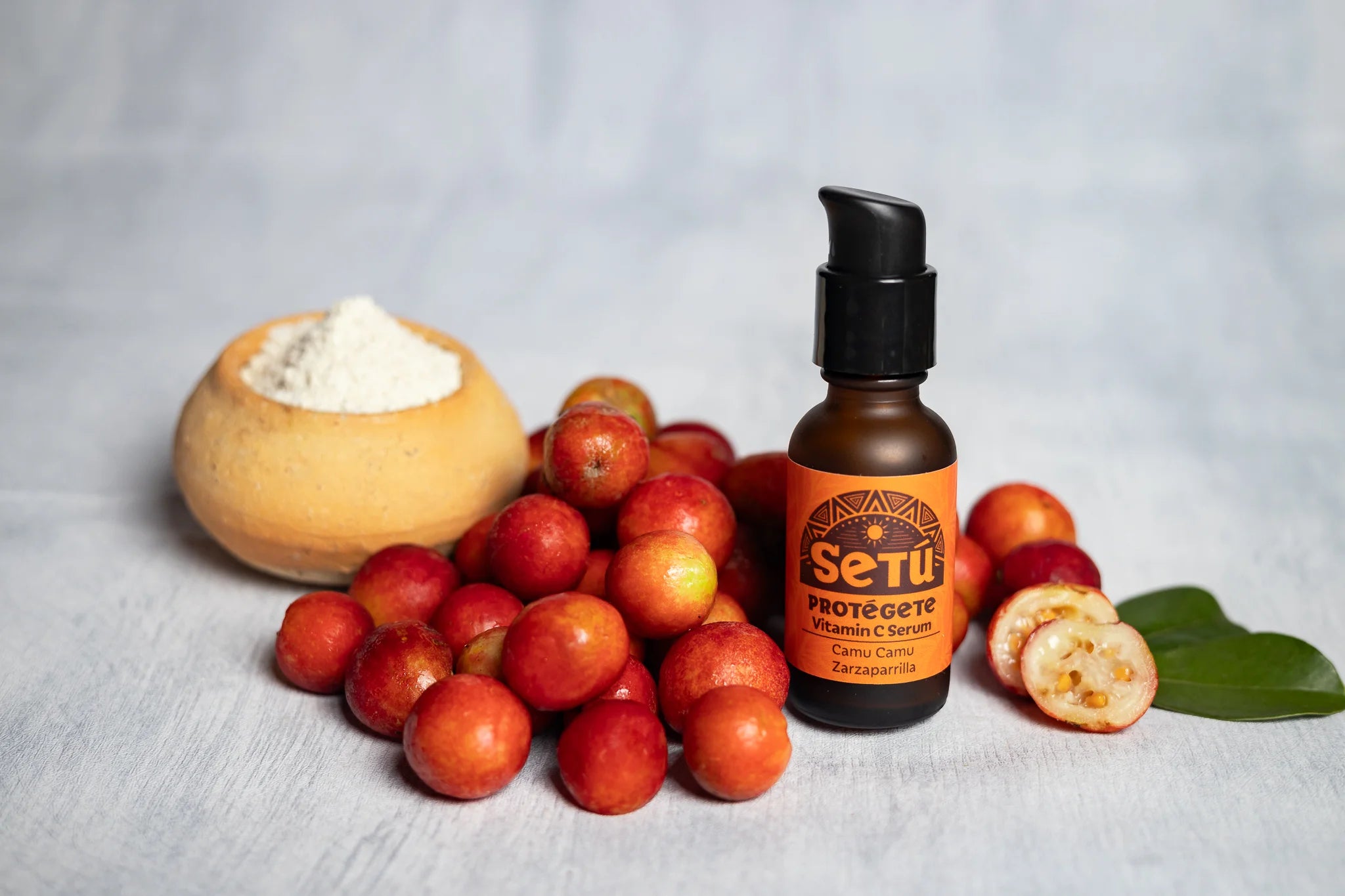 Bottle of Setu with camu camu fruits and a leaf on a gray background
